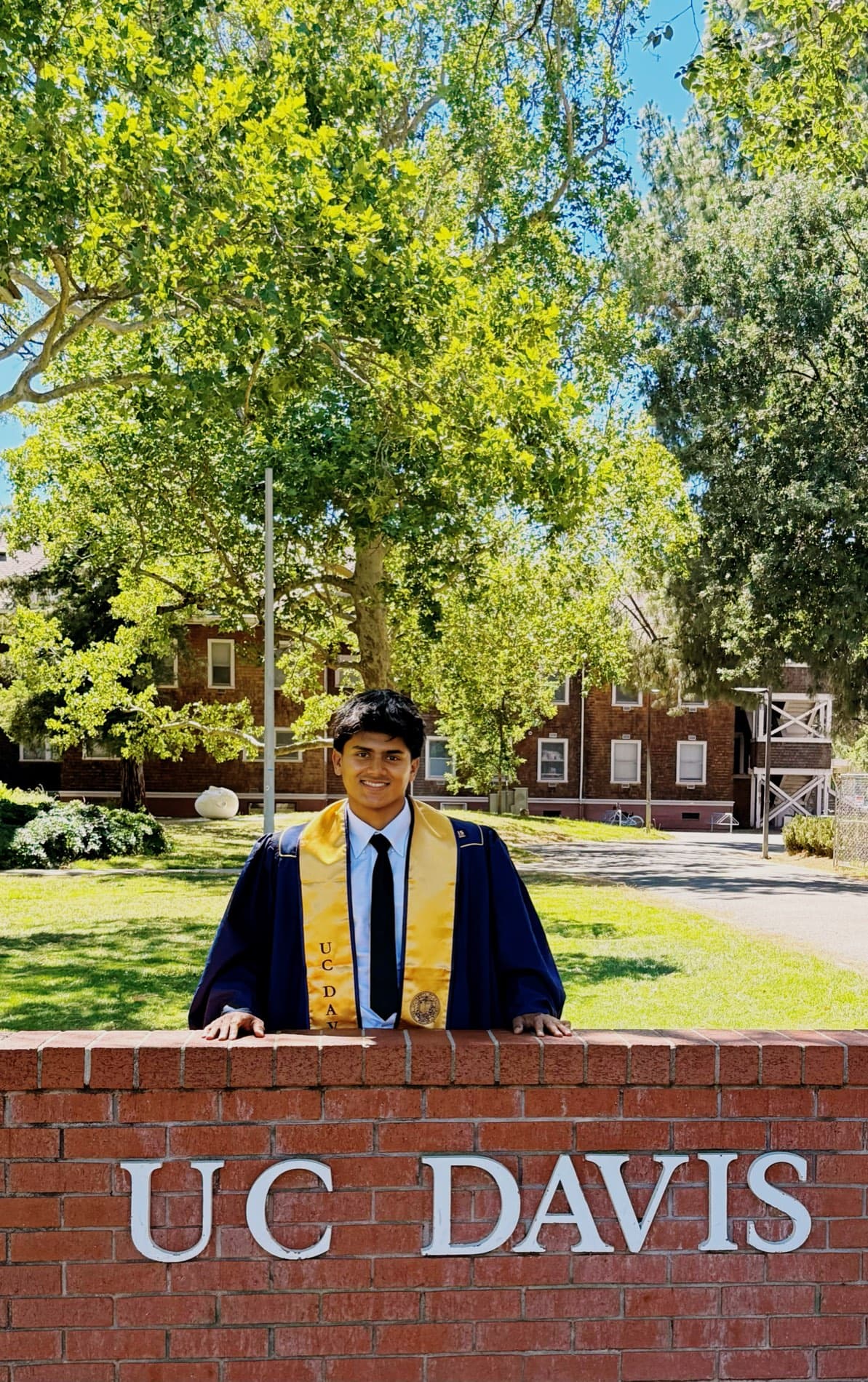 Jameel Jamhar in graduation regalia at the UC Davis campus sign